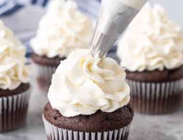 Piping stabilized whipped cream on top of a chocolate cupcake.