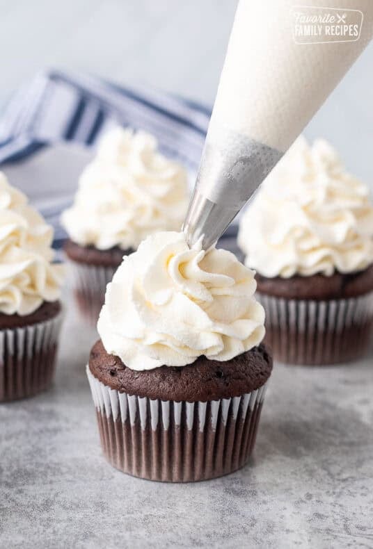 Piping stabilized whipped cream on top of a chocolate cupcake.