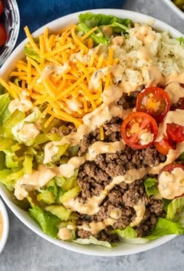 Burger Salad in a bowl with lettuce, hamburger meat, cherry tomatoes, grilled onions, cheddar cheese, chopped dill pickles and special sauce dressing.