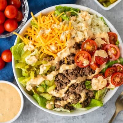 Burger Salad in a bowl with lettuce, hamburger meat, cherry tomatoes, grilled onions, cheddar cheese, chopped dill pickles and special sauce dressing.