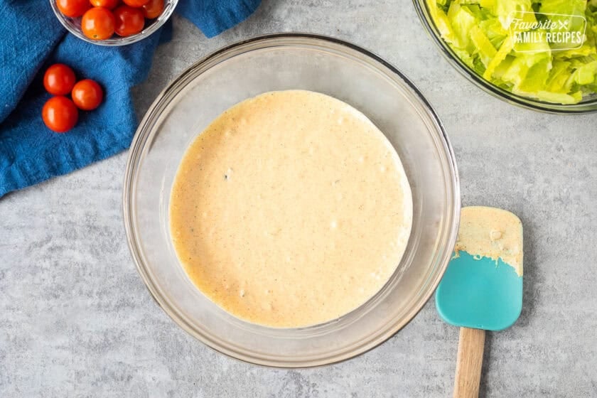 Glass mixing bowl with burger salad dressing with spatula on the side.
