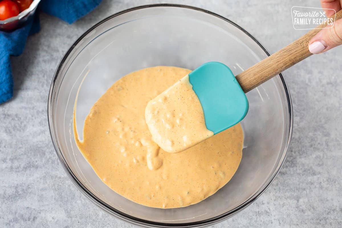 Glass mixing bowl with chilled burger salad dressing and spatula.