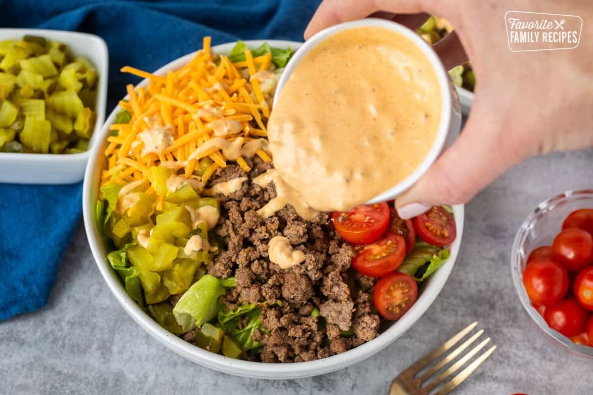 Pouring special sauce dressing onto burger salad.