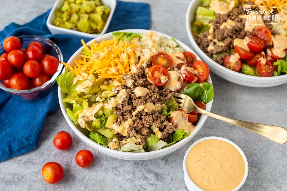 Burger Salad in a bowl with lettuce, hamburger meat, cherry tomatoes, grilled onions, cheddar cheese, chopped dill pickles and special sauce dressing.