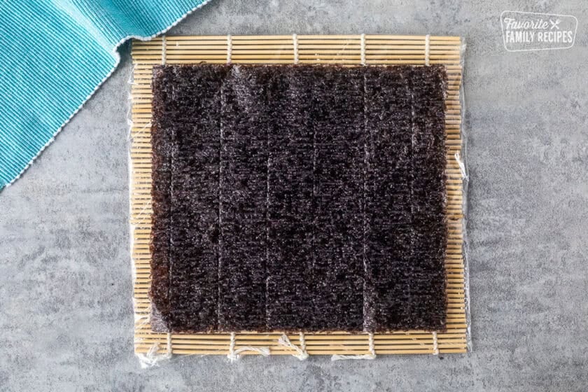 Bamboo mat covered in plastic wrap with a piece of nori on top.