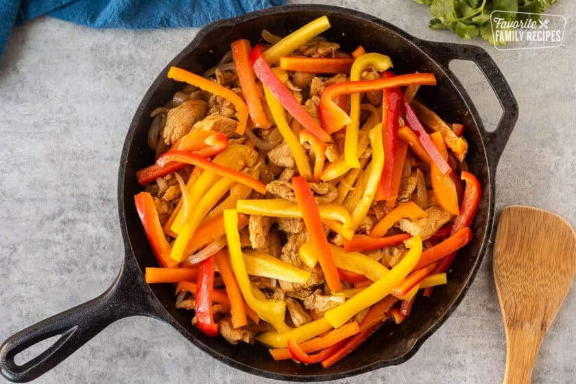 Skillet with marinated cooked chicken, onion and bell peppers for chicken fajitas.