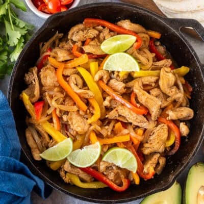 Skillet for chicken fajitas with marinated chicken, onion and bell peppers. Sides of flour tortillas, avocado, sour cream limes, cilantro and tomatoes.