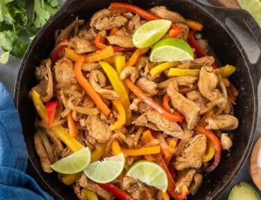 Skillet for chicken fajitas with marinated chicken, onion and bell peppers. Sides of flour tortillas, avocado, sour cream limes, cilantro and tomatoes.