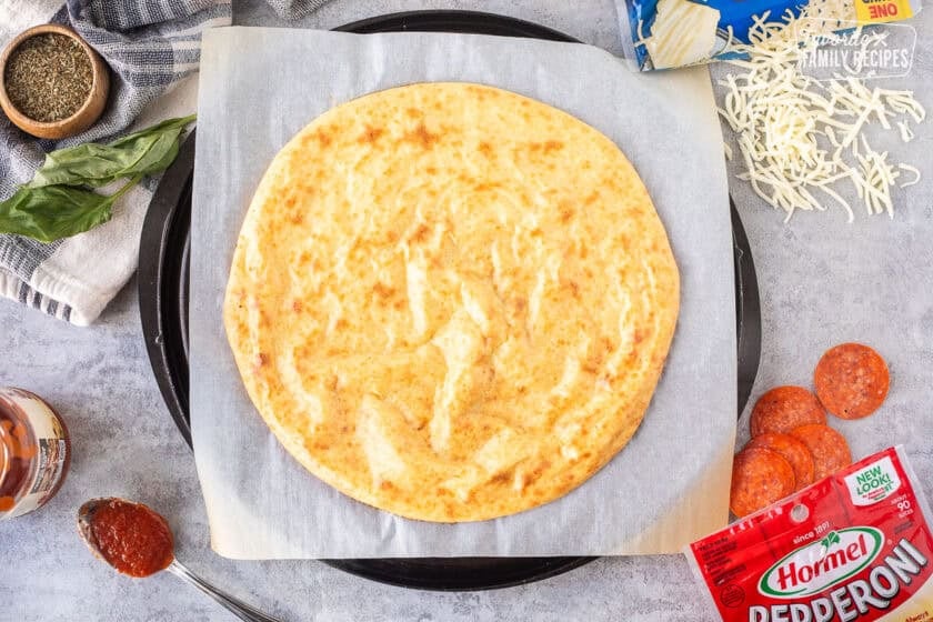 Baked cottage cheese pizza crust on parchment paper with toppings around.
