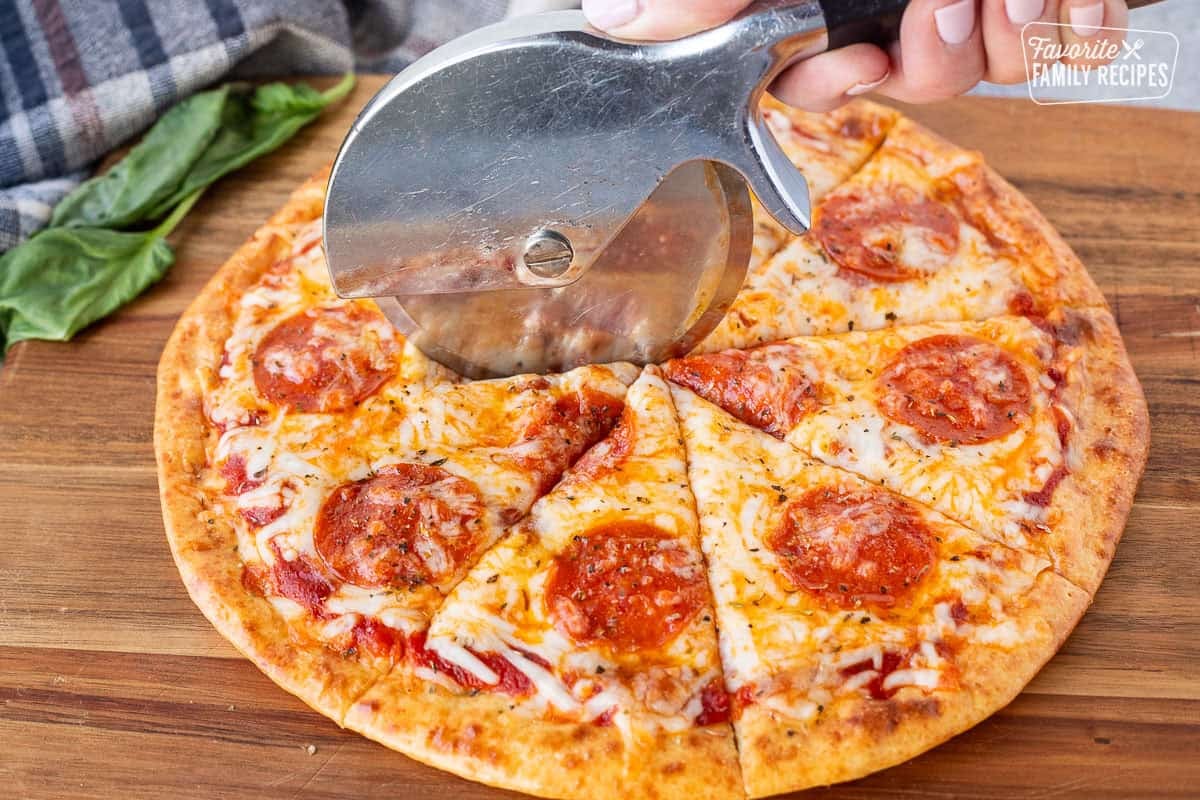 Cutting pepperoni pizza on cottage cheese pizza crust with a pizza slicer.