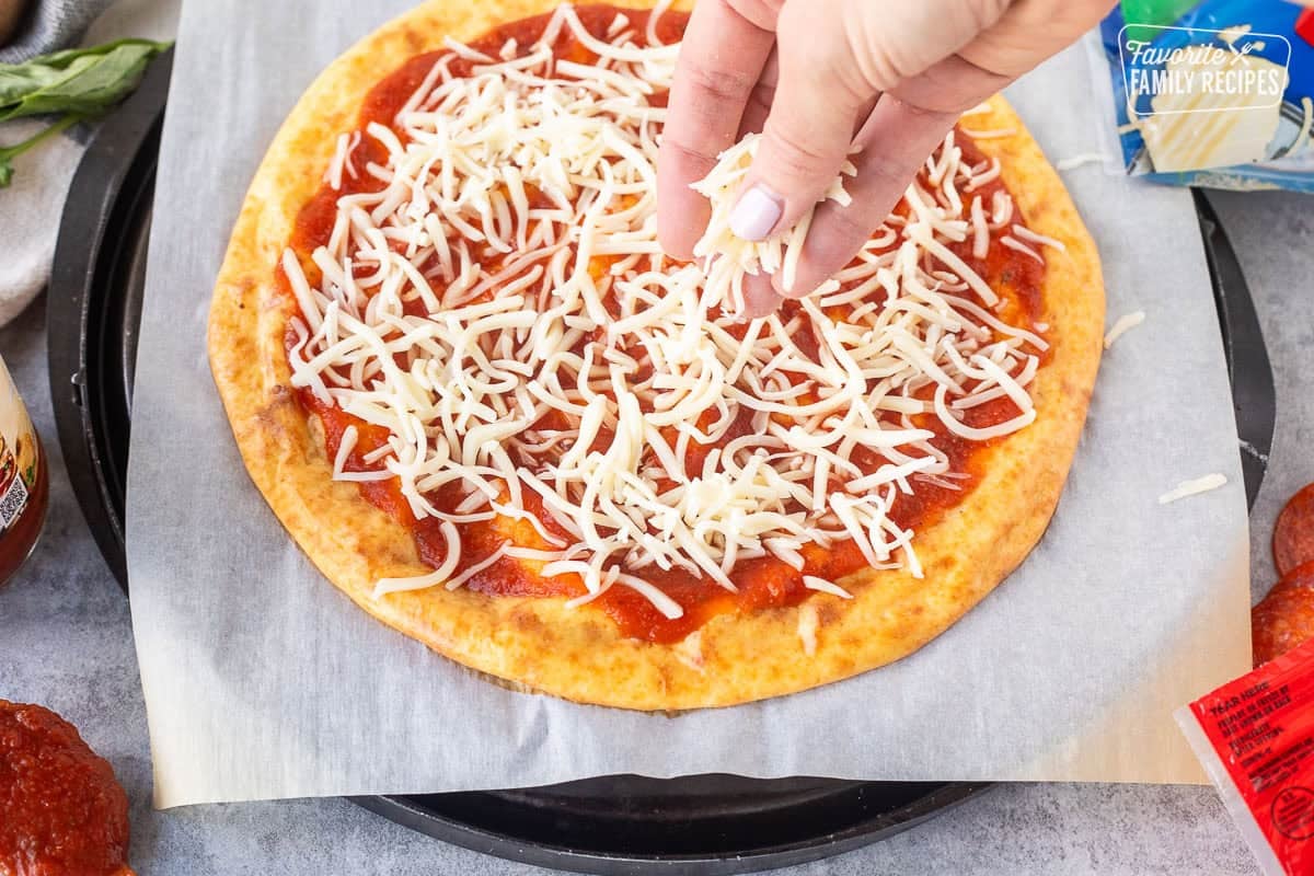 Sprinkling mozzarella cheese on top of cottage cheese pizza crust with pizza sauce.