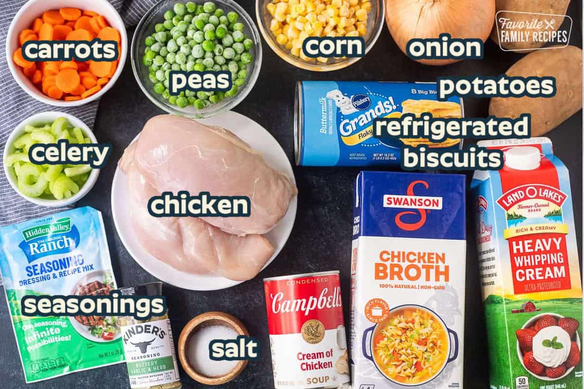 Ingredients to make crock pot chicken pot pie including potatoes, onion, heavy whipping cream, chicken broth, cream of chicken, grands biscuits, frozen corn, frozen peas, sliced carrots, sliced celery, chicken breast, salt, garlic butter seasoning, and Ranch dressing mix.