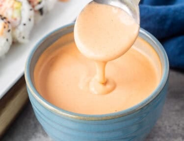 Drizzling easy sriracha mayo from a spoon into a bowl.