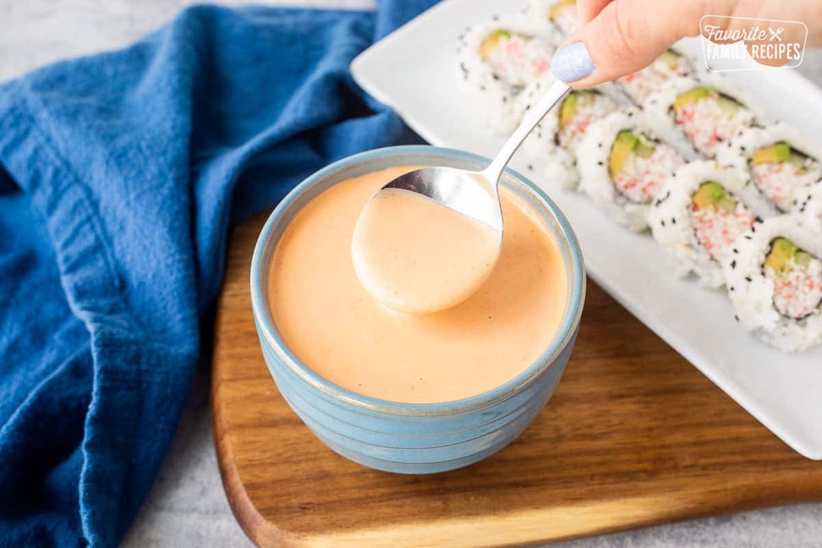 Bowl with easy sriracha mayo and spoon next to a plate with sushi.