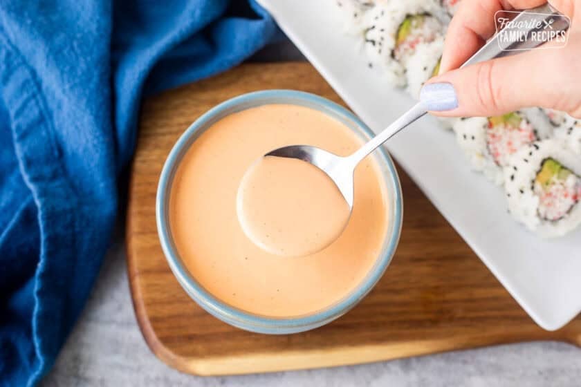 Spoon of easy sriracha mayo over a bowl. Sushi on the side.