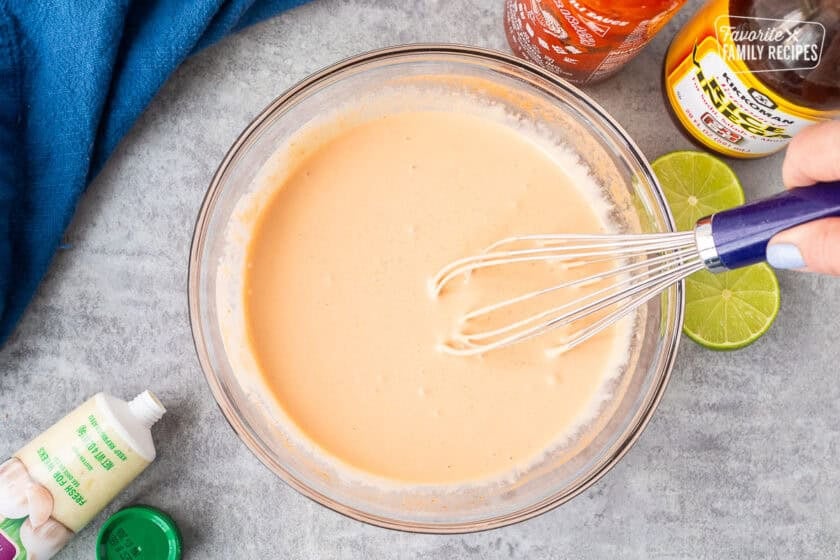 Whisking together easy sriracha mayo in a glass bowl with a whisk.