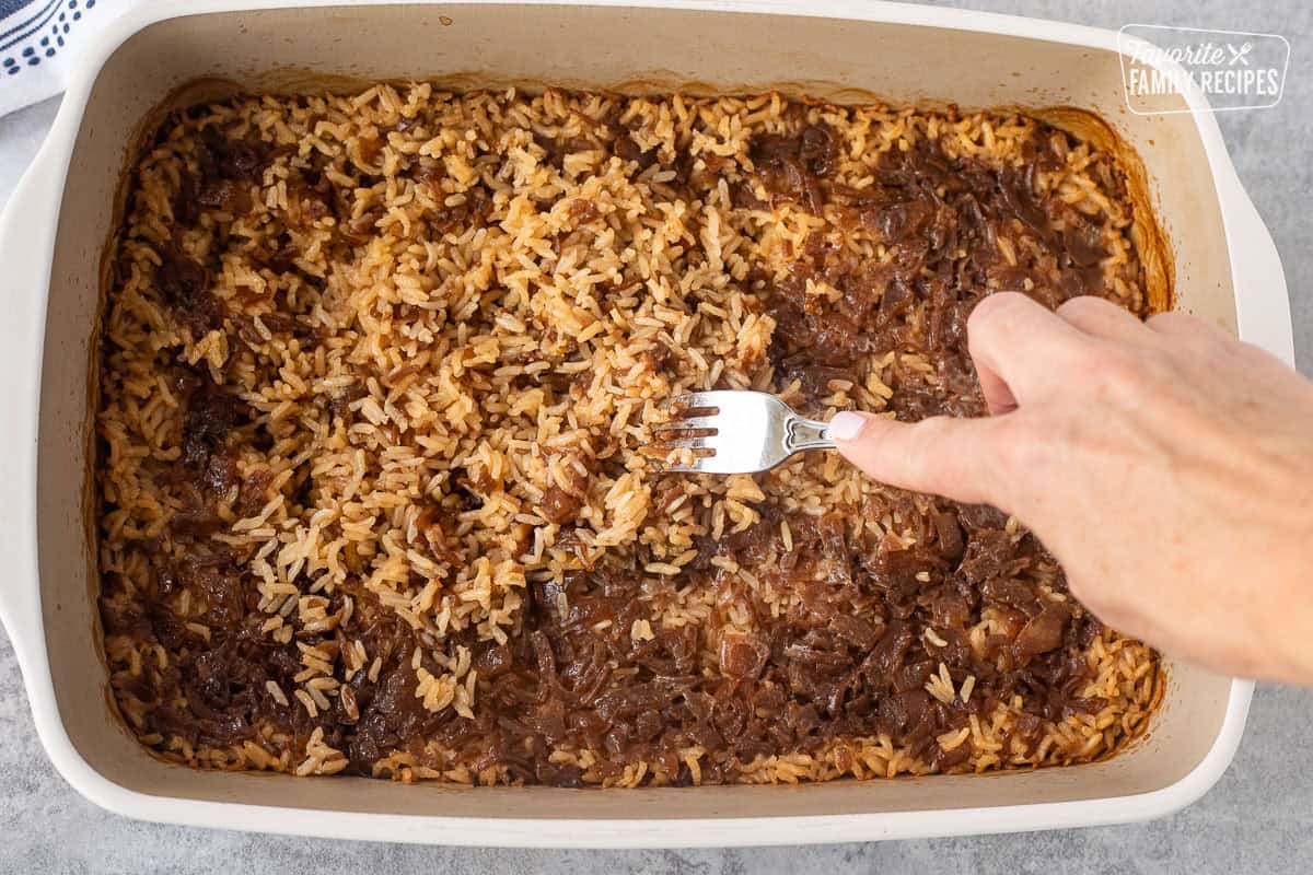 Fluffing French onion rice with a fork in a baking dish.