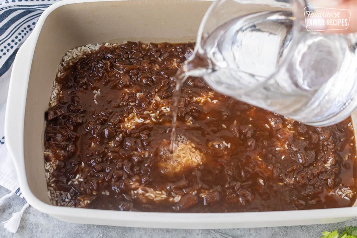 Pouring water into baking dish of French onion soup and rice to make French onion soup rice side dish