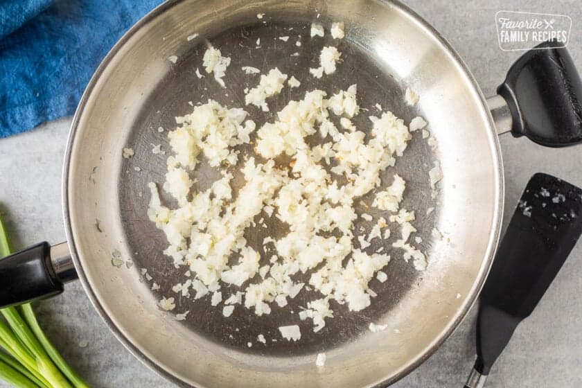 Skillet with cooked onion and garlic. Spatula on the side.