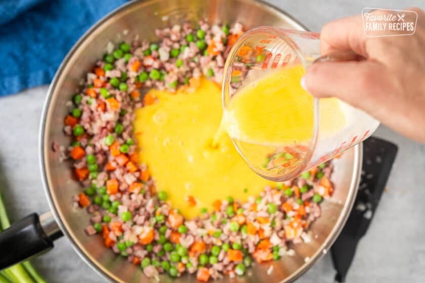Pouring lightly whisked egg into middle of skillet around ham and vegetables.
