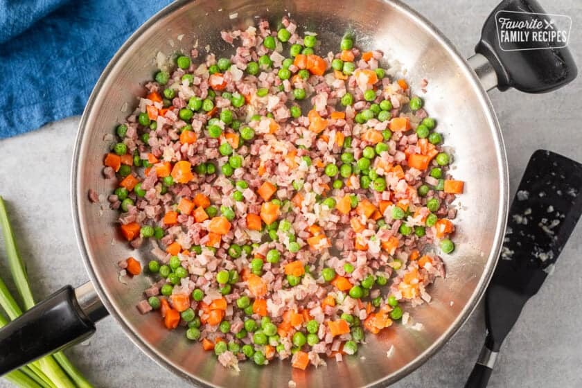 Skillet with cooked ham, carrots and peas. Spatula on the side.