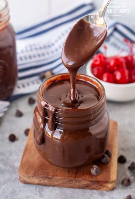 Drizzling hot fudge sauce into a jar with a spoon.