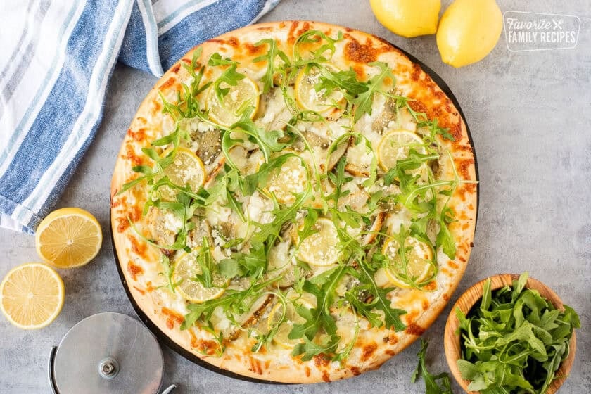 Lemon chicken pizza with cheesy lemon white sauce, mozzarella cheese, artichoke hearts, lemon chicken, lemon slices, feta cheese and fresh arugula.