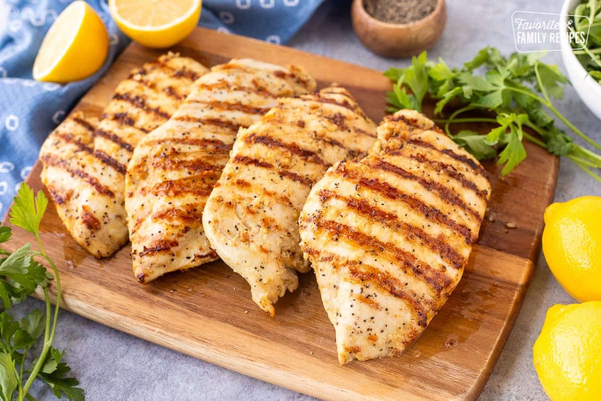 Four grilled lemon pepper chicken breasts on a cutting board.