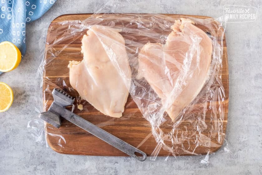 Pounding chicken breasts covered with plastic wrap thin with a metal mallet.
