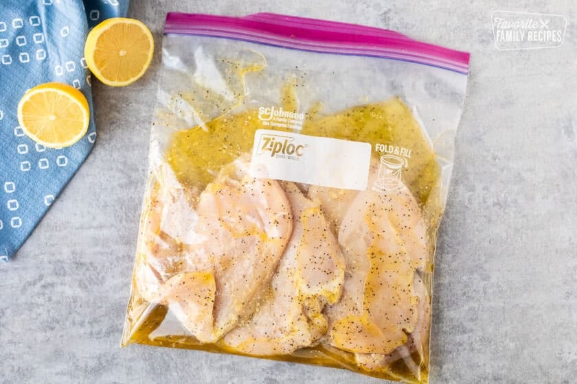 Chicken breasts marinating with lemon pepper seasonings in a ziplock bag.