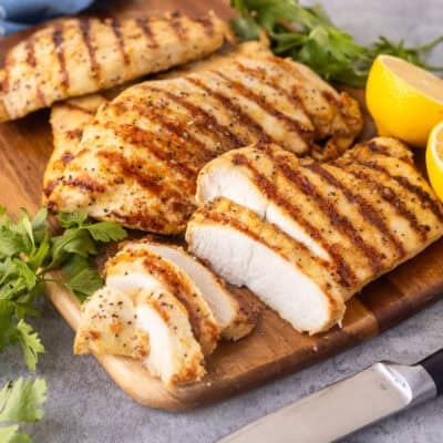 Sliced lemon pepper chicken on a cutting board with a knife.