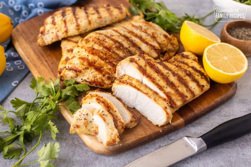 Sliced lemon pepper chicken on a cutting board with a knife.