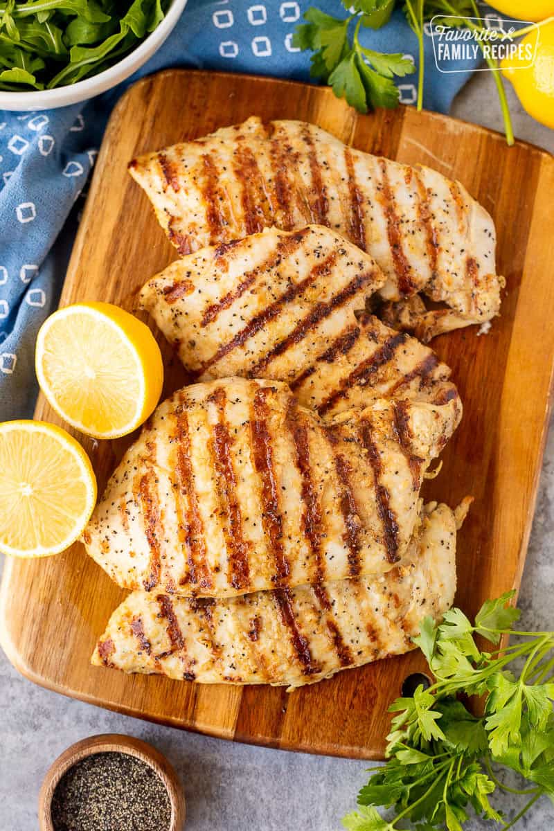 Four grilled lemon pepper chicken breasts on a cutting board.