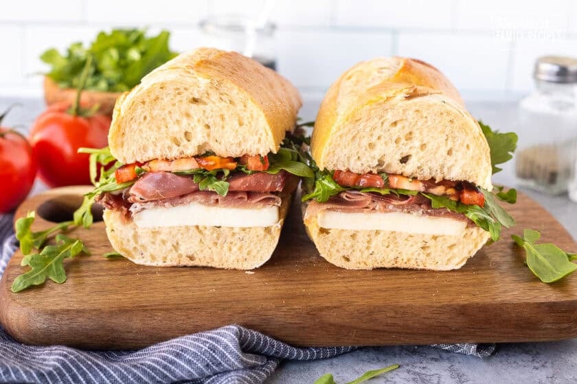 Prosciutto sandwich cut in two on a cutting board.