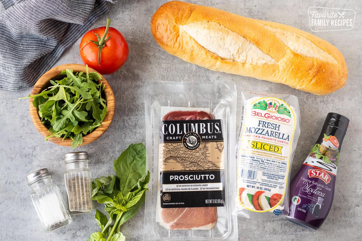 Ingredients to make prosciutto sandwich including Demi French bread, balsamic glaze, mozzarella cheese, prosciutto, basil, arugula, tomato, salt and pepper.