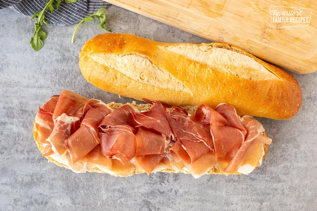 Demi French bread cut in half with a layer of fresh thick cut mozzarella cheese and prosciutto.