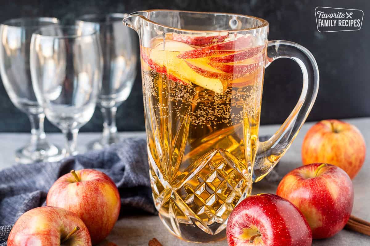 Sparkling cider in a glass pitcher with fresh sliced apples floating on the top.