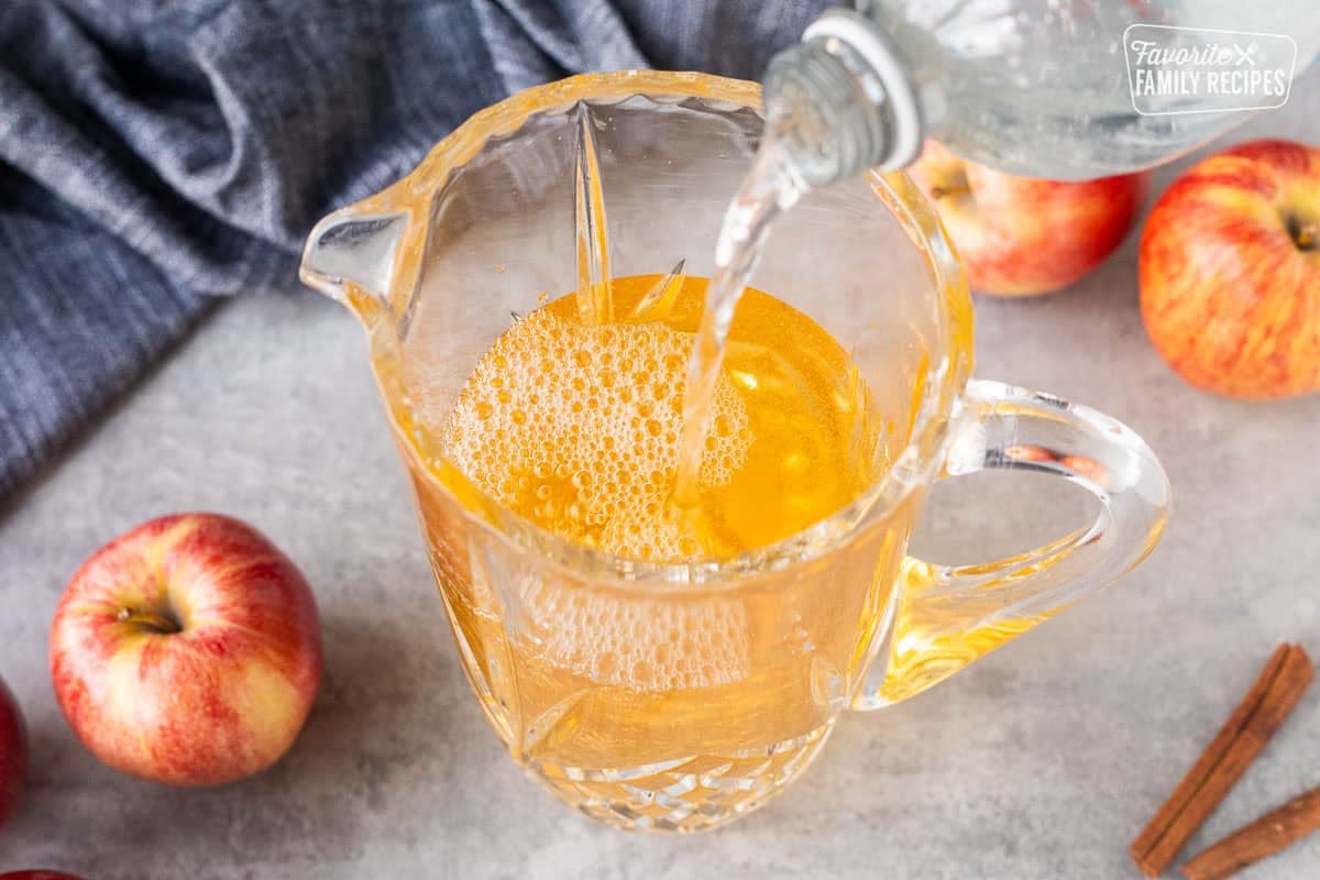 Pouring club soda into a glass pitcher with apple cider.