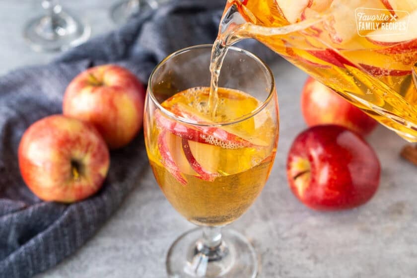Pouring sparkling cider into glass with sliced apples.
