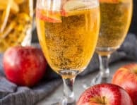 Two glasses of sparkling cider with fresh apple slices floating on top.