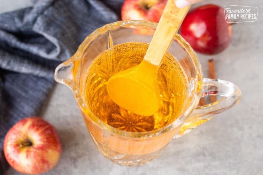 Stirring sparkling cider in pitcher with a spoon.