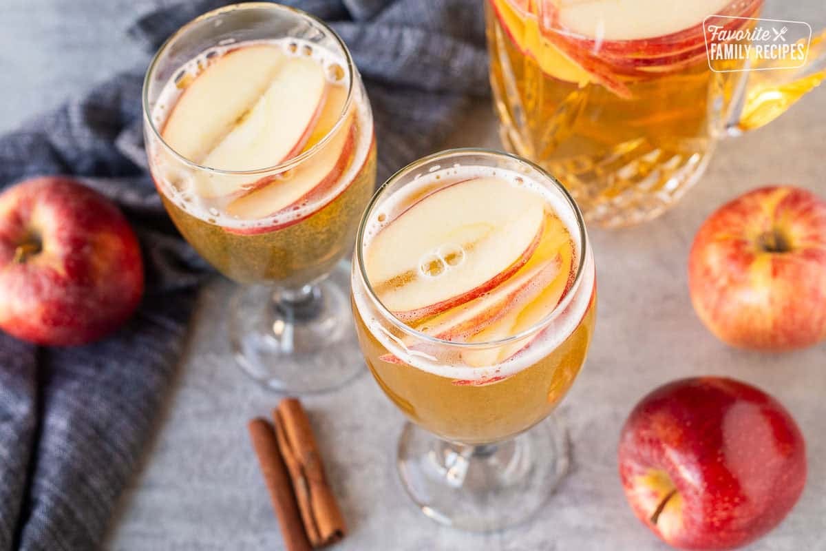 Sparkling cider in two glasses with floating apples.