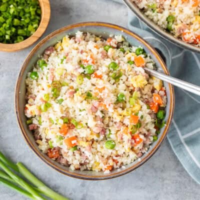 Bowl of cauliflower fried rice next to skillet and garnished with green onions.