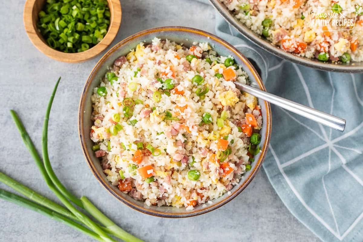 Bowl of cauliflower fried rice next to skillet and garnished with green onions.