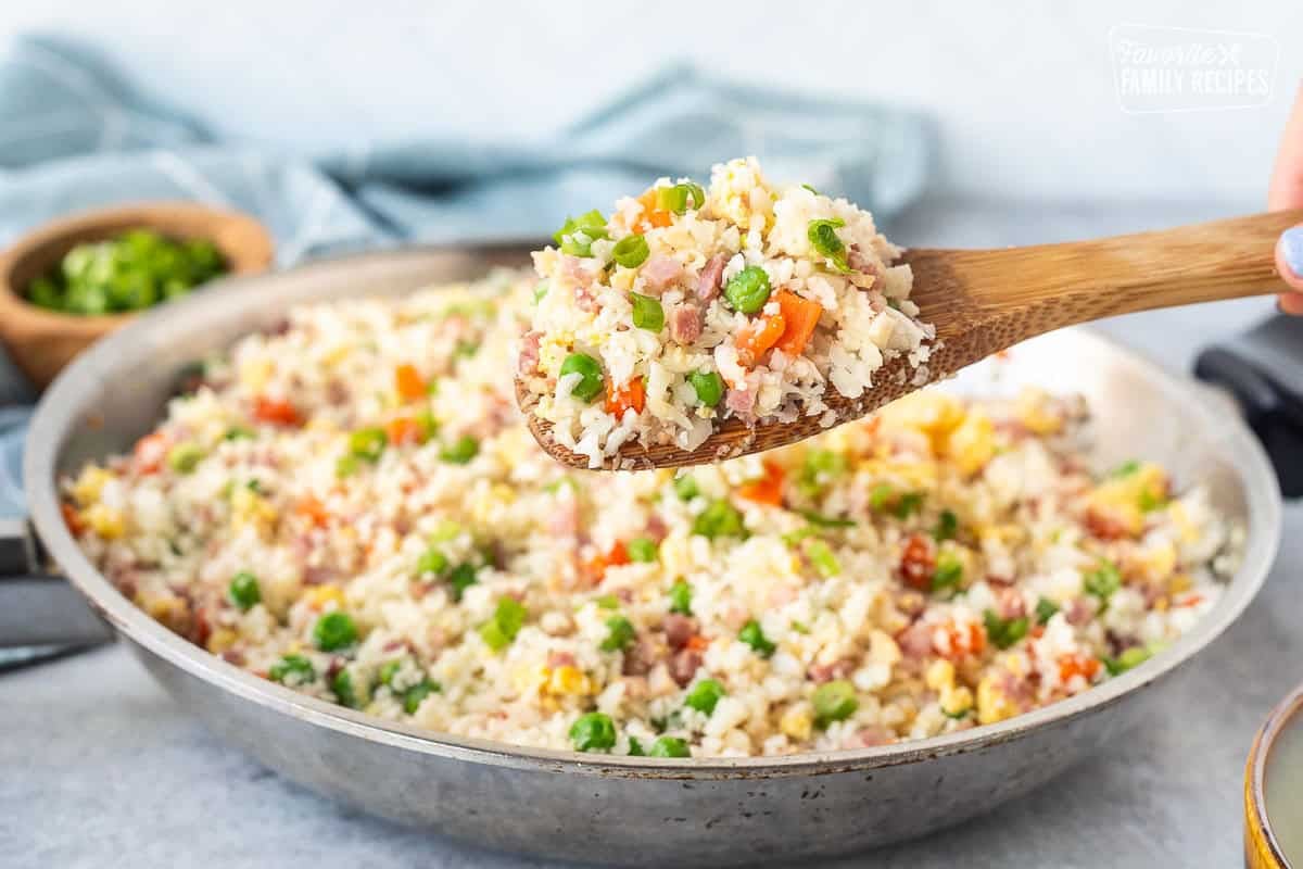 Cauliflower fried rice in a wooden spoon over a skillet.