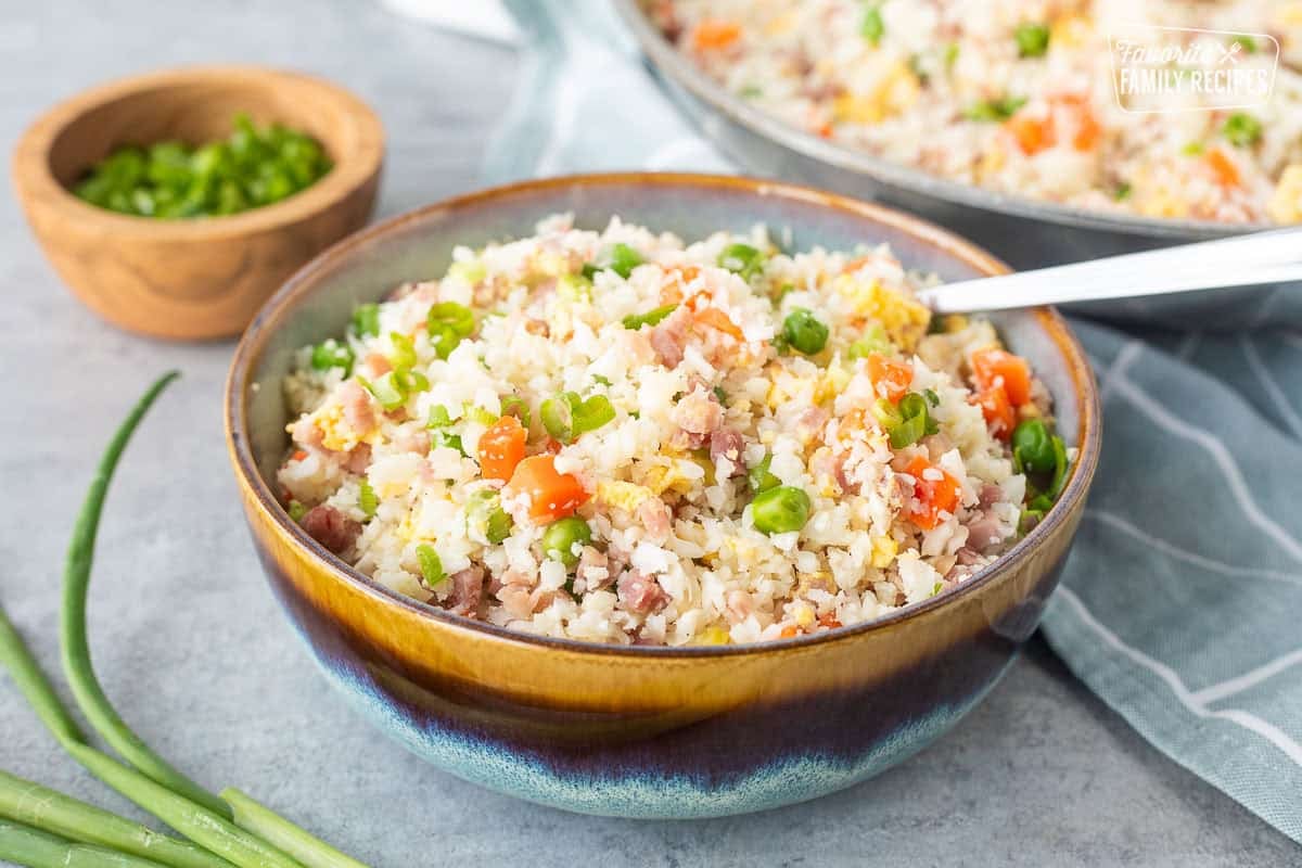 Bowl of cauliflower fried rice next to skillet and garnished with green onions.