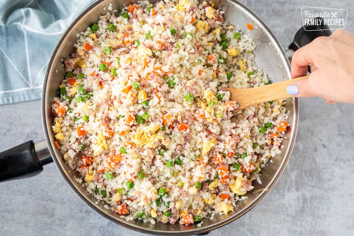 Mixing in cauliflower rice with ham, peas and carrots.