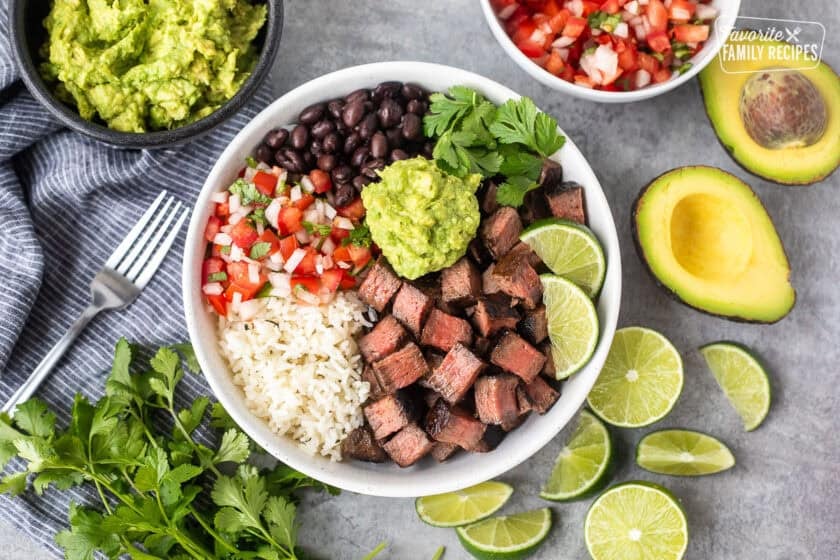 Chipotle steak bowl with rice, black beans, pico, guacamole, lime wedges and cilantro.