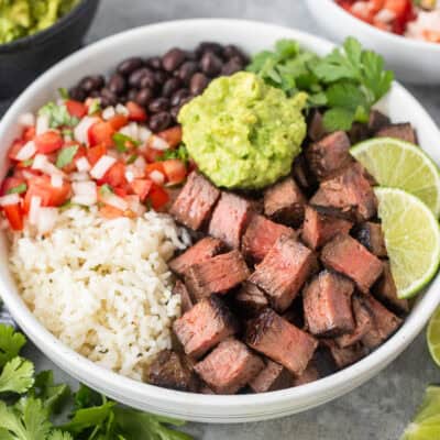 Chipotle steak with rice, black beans, pico, guacamole, lime wedges and cilantro.