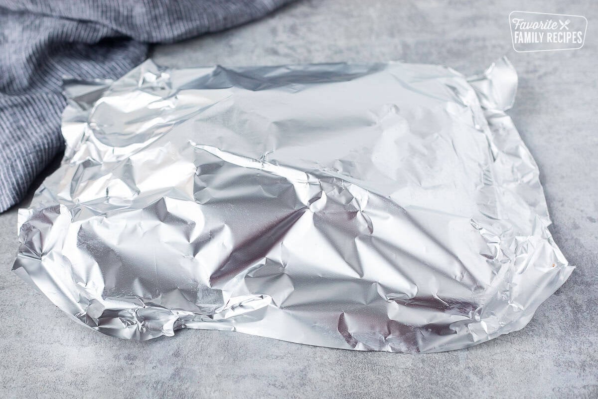 Covering Chipotle steaks with foil on a cutting board.